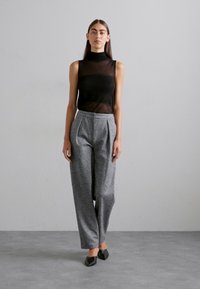 Schwarzes ärmelloses Rollkragenoberteil; hochtaillierte graue Karohose mit Falten; elegante schwarze Schuhe; strukturierte Oberfläche; neutraler Hintergrund.