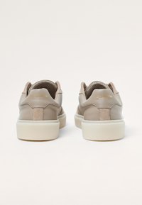 Zapatillas de cuero beige con acentos texturizados, suela de goma blanca y branding dorado en el talón. Punta redondeada y construcción resistente.