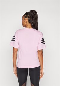 Lyserød bomulds t-shirt med sorte striber på ærmerne, rund halsudskæring og afslappet pasform. Båret med sorte legginger, der viser en glat tekstur.