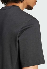 Černé tričko s krátkým rukávem vyrobené z bavlny, s klasickým střihem u krku a jemnou texturou s čistým zakončením švů.