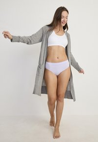 Jasnoszary kardigan na białym staniku sportowym i liliowych majtkach. Kardigan ma kieszenie i luźny krój, podkreślając warstwowy wygląd.