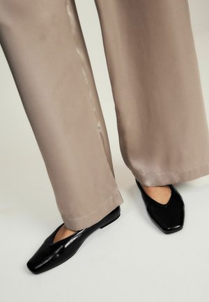 Legs wearing beige wide-leg pants and black square-toe flats on a light background.