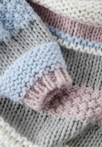 Stora megzta medžiaga pastelinių spalvų: šviesiai mėlyna, rožinė, pilka ir kreminė. Su tekstūruotomis juostelėmis ir briaunotomis kraštinėmis papildomam detalumui.