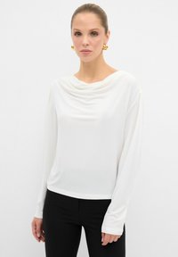 Witte langemouwen top met een gedrapeerde halslijn. Glad, lichtgewicht stof met een ontspannen pasvorm. Gecombineerd met zwarte, aansluitende leggings.