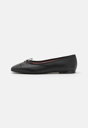 Zapatilla bailarina de cuero negro con punta redondeada, tacón bajo y pequeño lazo decorativo en la parte superior, mostrada de perfil sobre un fondo blanco.