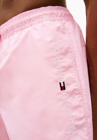 Pantaloni da bagno rosa realizzati in un tessuto leggero e liscio. Presentano una vita elasticizzata e un logo ricamato con accenti rosso, bianco e blu.