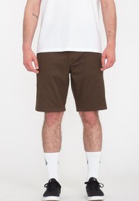 Brune shorts med en klassisk pasform, flad frontdesign, syede kanter og sidelommer, parret med hvide sokker og sorte sneakers.