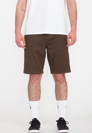 Bruine shorts met een klassieke pasvorm, een vlakke voorkant, gestikte zomen en zijzakken, gecombineerd met witte sokken en zwarte sneakers.