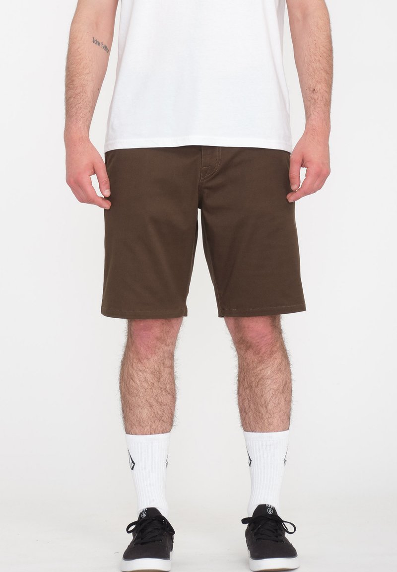 Brune shorts med en klassisk pasform, flad frontdesign, syede kanter og sidelommer, parret med hvide sokker og sorte sneakers.