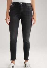 Jean skinny noir avec un ourlet effiloché, fabriqué en tissu denim. Associé à des baskets blanches avec des accents argentés pour le contraste.