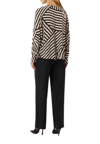 Blusa a maniche lunghe a righe bianche e nere con motivo geometrico, abbinata a pantaloni neri a gamba dritta e décolleté nere a punta.