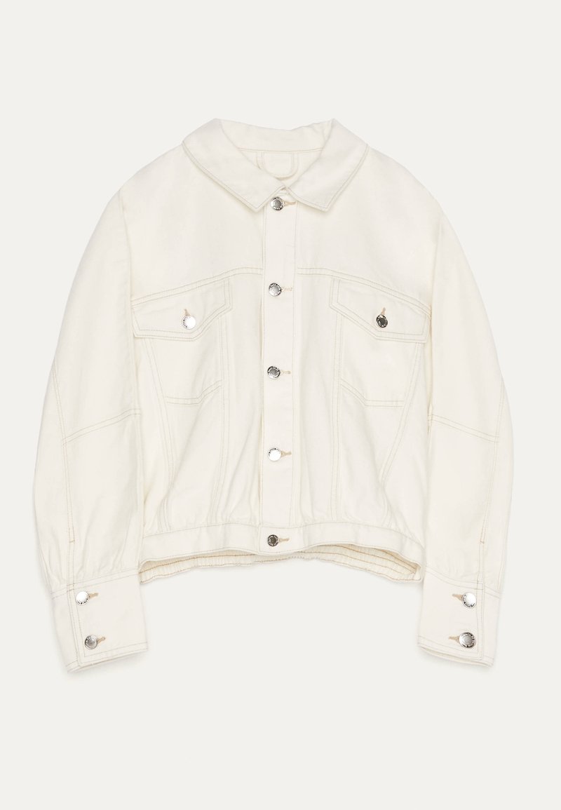 Off-white denim jacket with silver snap buttons, chest flap pockets, buttoned cuffs, and a classic collar, laid flat on a white background.