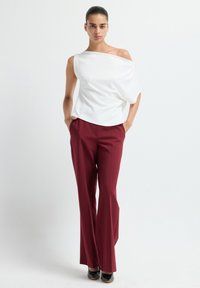 Top bianco scollato con tessuto drappeggiato, abbinato a pantaloni bordeaux a vita alta, con gamba larga. Scarpe con tacco nere completano l'outfit.