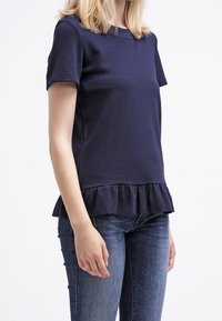 Haut bleu marine à manches courtes, avec un détail de bord effilé et une texture lisse ; associé à un jean ajusté. Aucune motif ou matériel visible.