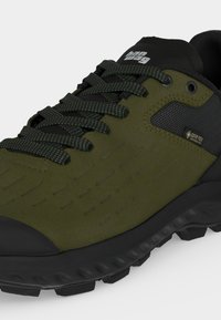 Πράσινο και μαύρο ορειβατικό παπούτσι Gore-Tex με κορδόνια με σχέδια, υφασμένο σουέτ επάνω μέρος και ανθεκτική μαύρη σόλα για εξωτερική χρήση.