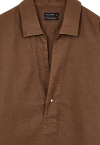 Camicia di lino marrone con colletto, abbottonatura frontale con un solo bottone e vestibilità sagomata. Tessuto texture con un leggero lucido.