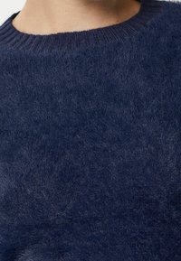 Pull en bleu marine avec une texture douce et duveteuse et un col rond côtelé. Le tissu semble léger et confortable, idéal pour un usage décontracté.