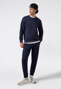 Conjunto de sudadera y pantalones en color azul marino, hecho de una tela suave. Presenta puños elásticos, un cuello redondo y acentos de logo. Se lleva con zapatillas ligeras.