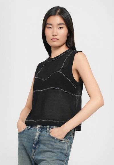 Haut sans manches noir avec un design en tricot texturé, featuring des coutures blanches contrastantes en motifs géométriques. Porté avec un jean en denim bleu clair.