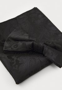 Pajarita negra hecha de un tejido con patrón y textura suave, colocada sobre un pañuelo de bolsillo negro a juego con un sutil diseño de cachemira.