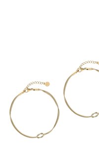 Orecchini a cerchio in oro con un design liscio, dettagli intrecciati e una piccola catena per la lunghezza regolabile. Finitura in metallo testurizzato.