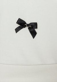 White fabric with a textured surface features a small black satin bow at the center, secured by metal hardware details.