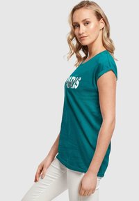 Türkise Baumwoll-T-Shirt mit kurzen, aufgerollten Ärmeln, das ein grafisches Textdesign mit der Aufschrift "PARIS" in Weiß zeigt. Glatte Textur und lockere Passform.