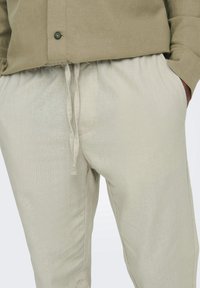 Helle beige Leinenhose mit elastischem Bund und Kordelzug. Verfügt über Seitentaschen und eine dezente Textur.