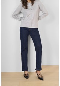 Graues langärmliges Hemd mit Knöpfen, dunkelblaue Jeans und schwarze spitze Absatzschuhe mit Riemchen. Glatte Stoffqualität und taillierte Passform.