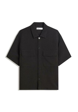 Zwarte shirt met korte mouwen van stof met een gladde textuur, voorzien van twee voorzakken, een klassieke kraag en een knoopsluiting.