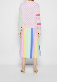 Flerfärgad stickad tröja med diamantmönster och randiga ärmar, i kombination med en plisserad kjol med pastellrand. Inomhusskor med gröna accenter.