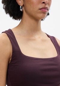 Σκούρο μωβ αμάνικο τοπ με τετράγωνη λαιμόκοψη, φτιαγμένο από μαλακό ύφασμα. Μεγάλες ασημί κρίκοι σκουλαρίκια συμπληρώνουν το σχέδιο.