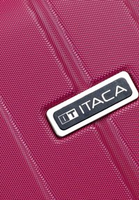 Maleta rígida de color rosa oscuro brillante, con una superficie texturizada y estrías, y una placa de logo plateada etiquetada "IT ITACA."