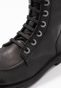Black leather boot with a smooth texture, flat black laces, and metal eyelets. Features a round toe and a stitched sole for durability.