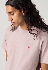 Lichtroze T-shirt met korte mouwen, gemaakt van zachte stof, met een klein rood Levi's-logo op de linkerkant van de borst. Gladde textuur, klassieke pasvorm.