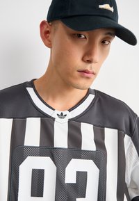 Mustra mustriga mustar ja valge spordijersey, millel on võrgusilmast tekstuur, julge number 92 ja valge krae, millel on kaelal Adidas'i logo.