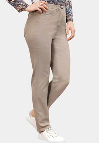 Pantalons en mélange de coton beige avec une coupe slim, un design à cinq poches et une fermeture à bouton. Associés à des baskets blanches et un haut à motifs.