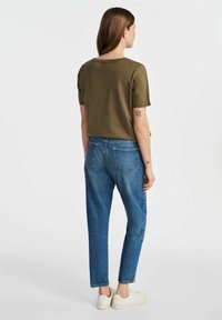 Oliwkowa bluzka na krótki rękaw zestawiona z niebieskimi dżinsami o wysokim stanie. Dżinsy mają tradycyjne tylne kieszenie i luźny krój.