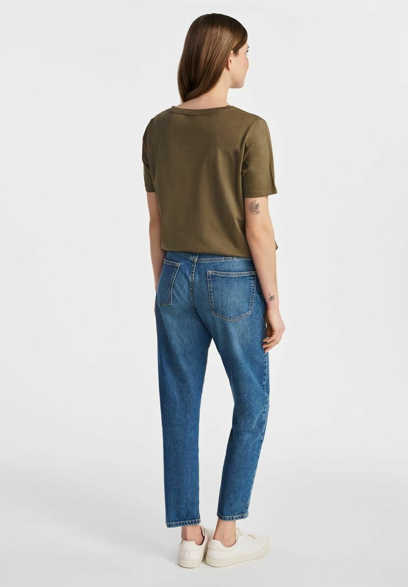 Oliwkowa bluzka na krótki rękaw zestawiona z niebieskimi dżinsami o wysokim stanie. Dżinsy mają tradycyjne tylne kieszenie i luźny krój.