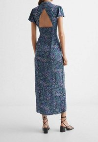 Maxi-mekko tummansinisestä kankaasta, jossa on kukkakuvioita, lyhyet hihansuut, selässä aukko ja istuva silhouette. Yhdistetty mustiin sandaaleihin.