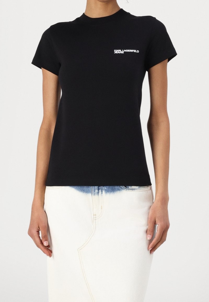 Svart bomull t-shirt med korta ärmar, rundad halsringning och en vit Karl Lagerfeld-logotyp på vänster bröst. Kombinerad med en ljus denimkjol.