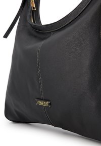 Black leather handbag with a pebbled texture, gold hardware accents, and contrasting white stitching. Features a logo tag on the side.