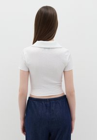 Korte mouwen, witte, gestructureerde crop top met een kraag, gecombineerd met donkerblauwe broek met elastische taille. Eenvoudig ontwerp en casual pasvorm.