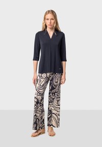 Top navy a tre quarti con scollatura a V, abbinato a pantaloni a gamba larga color crema con un audace motivo paisley nero.