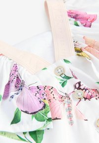 Kukkamekko valkoisella taustalla, jossa on vaaleanpunaisia ja purple perhosia. Kermansävyiset olkaimet, joissa on kohokuvioitu teksti, ja kaksi napinää kullatulla yksityiskohdalla.