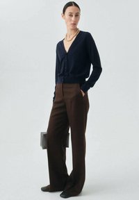 Cardigan navy con scollo a V, chiusura con bottoni e maniche lunghe abbinato a pantaloni larghi marroni e ballerine nere. Collana semplice in argento.
