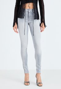 Tanke sivo denim hlače z visokim pasom, s petimi žepi in zbledelim videzom. Ujemajoče se s prosojno črno majico in petkami.