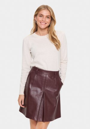 Cream sweater with long sleeves paired with a burgundy leather skirt featuring pleats and side pockets. Smooth texture and tailored fit.