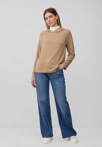 Beige trui met een capuchon, lange mouwen en een ontspannen pasvorm, gecombineerd met blauwe wijde jeans en witte sneakers. Eenvoudige, textuurstof.