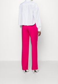 Witte, lange mouwen blouse met gathers aan de achterkant, gecombineerd met felroze, wijde broekspijpen en witte hoge hakken.